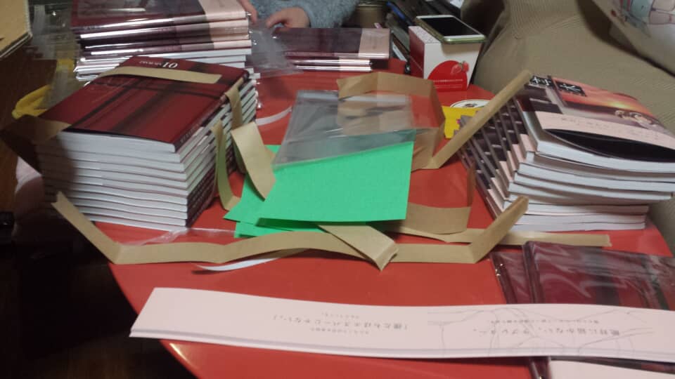 赤いテーブルの上に積まれた多数の冊子と梱包資材